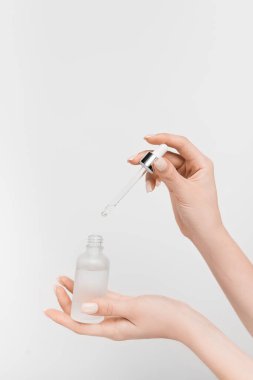 partial view of woman holding bottle with serum and pipette isolated on white clipart