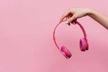 partial view of woman holding wireless headphones in hand isolated on pink clipart