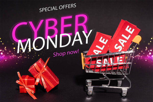 red gifts near toy cart with sale tags near special offers, cyber monday, shop now lettering on dark background, black friday concept