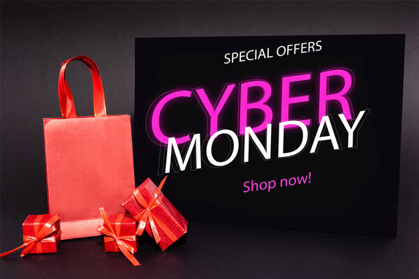 red presents and shopping bag near placard with special offers, cyber monday, shop now lettering on dark background