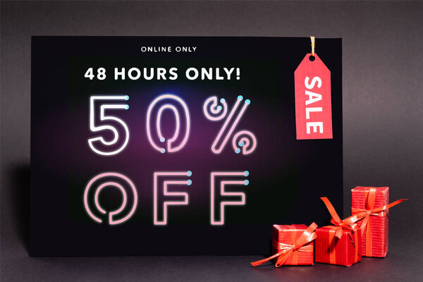 placard with online only, 48 hours only, 50 percent off lettering and sale tag near presents on dark background