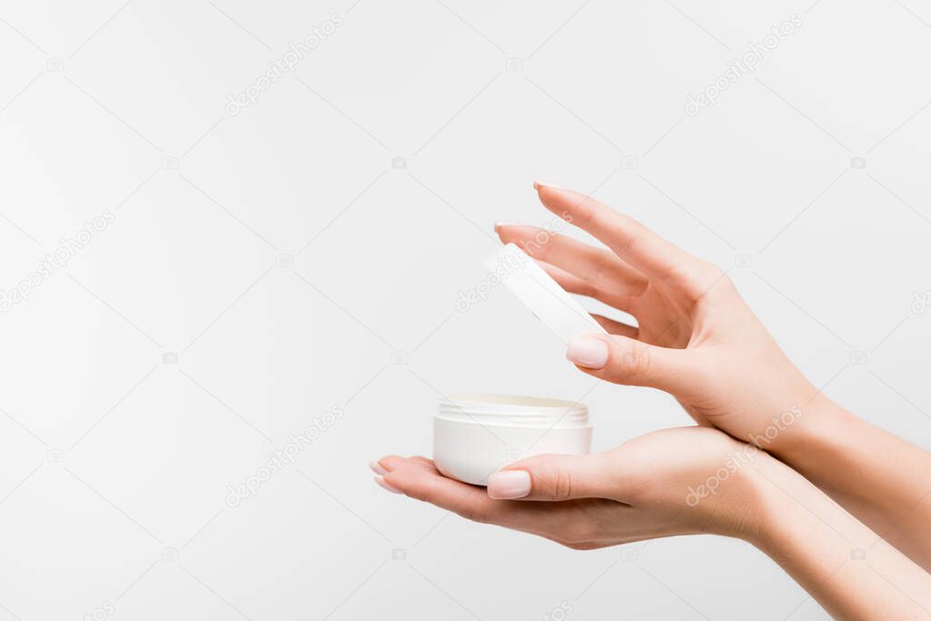 partial view of woman holding jar with cosmetic cream isolated on white