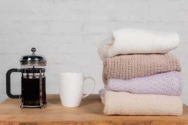 Cup and teapot near knitted sweaters on table on brick wall background clipart
