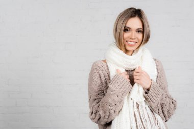 Smiling woman in knitted sweater and scarf looking at camera on white background clipart