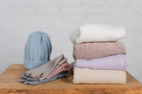 Woolen hat, sweaters and gloves on wooden table on white background