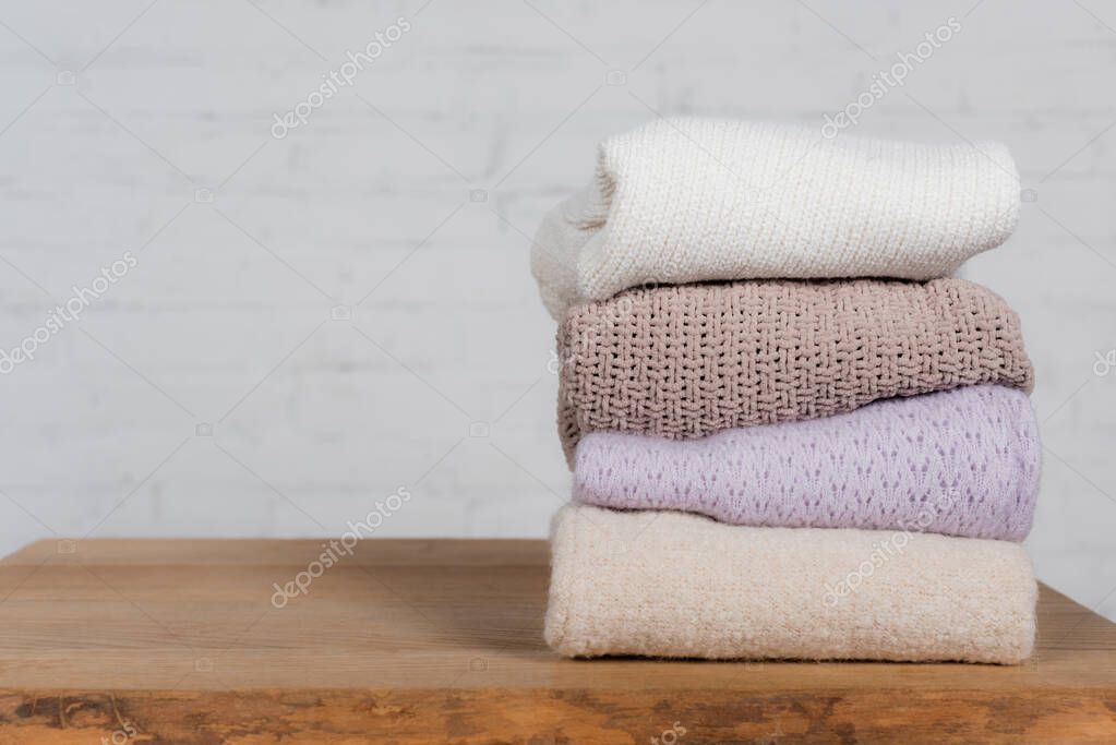 Warm and knitted sweaters on wooden table on white background