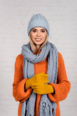 Young woman in warm hat, knitted sweater and gloves looking at camera on white background clipart