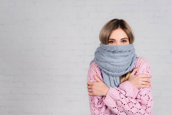 Woman in warm scarf and sweater suffering from cold on white background