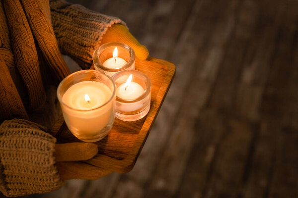 Cropped view of woman in knitwear and gloves holding burning candles on wooden board 