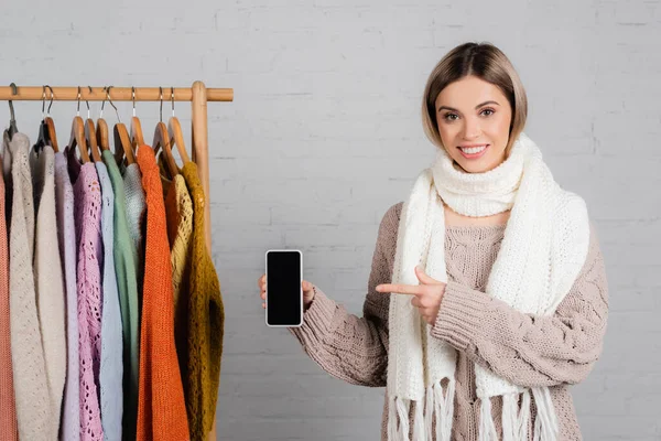 Smiling Woman Pointing Smartphone Blank Screen Hanger Rack Sweaters White — Stock Photo, Image