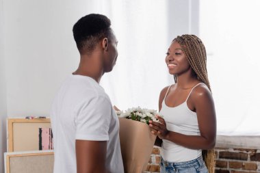 Gülümseyen Afrikalı Amerikalı kadın evde buketli sevgilisine bakıyor.