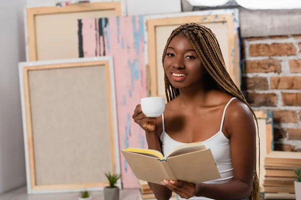 Lächelnde Afroamerikanerin Mit Tasse Und Buch Schaut Hause Die Kamera — Stockfoto