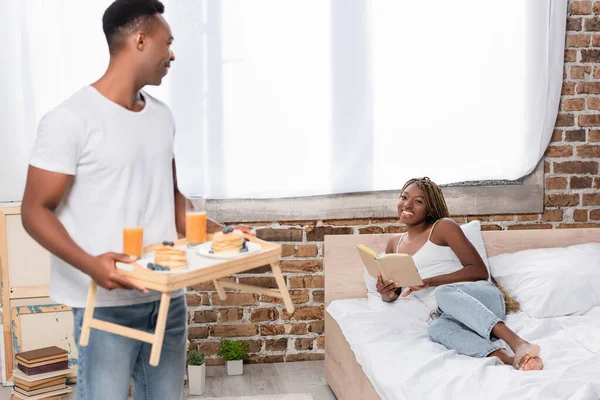 Sonriente Mujer Afroamericana Con Libro Mirando Novio Con Desayuno Bandeja — Foto de Stock