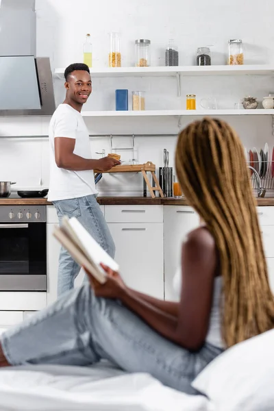 Smiling African American Man Holding Pancakes Tray Girlfriend Book Blurred — Stock Photo, Image