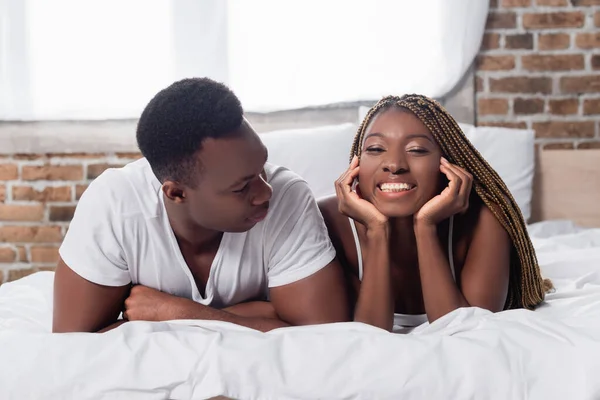 アフリカ系アメリカ人男見ています笑顔ガールフレンドオンベッド — ストック写真