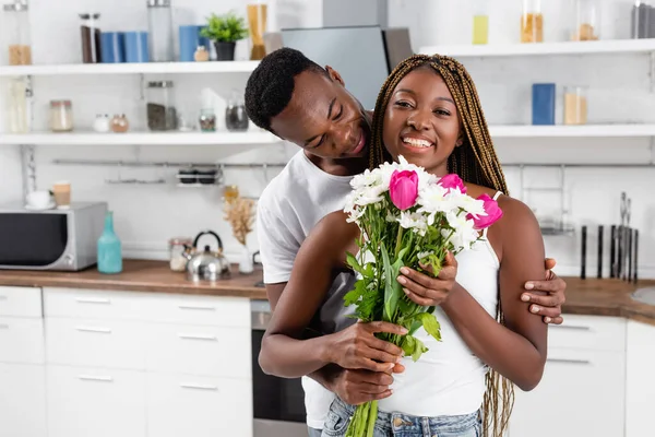 Africano Americano Homem Abraçando Alegre Namorada Com Buquê Cozinha — Fotografia de Stock