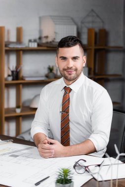 Mutlu mimar, iş yerinin yanında otururken kameraya bakıyor, bulanık ön plan