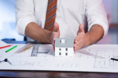 Mimarın evin modeline dokunuşunun kırpılmış görüntüsü masanın üzerinde, bulanık arkaplan