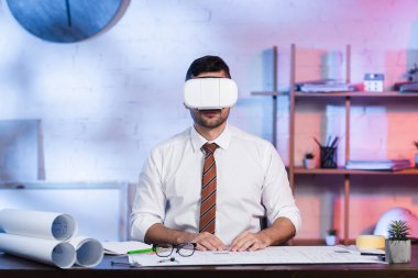 VR kulaklıklı mimar, iş yerinde şablonların yanında oturuyor.