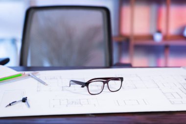 selective focus of eyeglasses and blueprint on desk in architectural agency, blurred background clipart