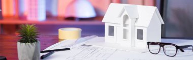 Gözlük ve planların yanındaki ev modeli mimarlık ajansında, pankartta.