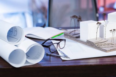 Ev modellerinin yanındaki gözlüklerin seçici odak noktası ve ofisteki masanın üzerindeki planlar, bulanık arkaplan