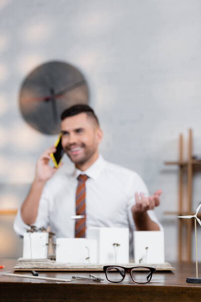 happy architect talking on mobile phone near architectural project, blurred background