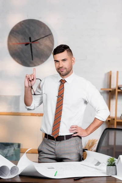 Arquitecto Sonriente Apuntando Hacia Arriba Con Dedo Mientras Está Pie — Foto de Stock