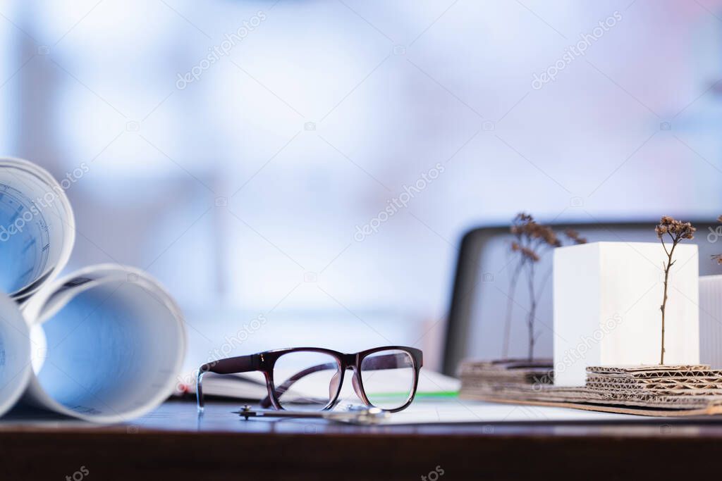 selective focus of eyeglasses near rolled blueprints on desk in office