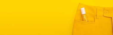 Sarı pankartla izole edilmiş pantolon cebinde tırnak cilası olan cam şişe manzarası.