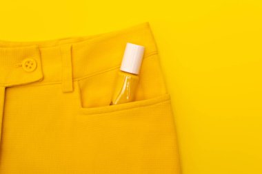 top view of glass bottle with nail polish in pocket of pants isolated on yellow clipart