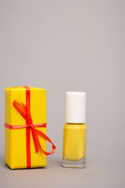 wrapped yellow gift box near bottle with nail polish isolated on grey clipart