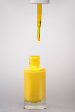 Sarı ojeli bir şişe ve gri arka planda fırça. 