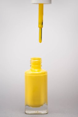 bottle with yellow nail polish and brush on grey background  clipart