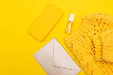 top view of bottle with nail polish, smartphone in case near clothing and envelope isolated on yellow  clipart