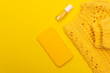 top view of bottle with nail polish, smartphone in case near jumper isolated on yellow  clipart