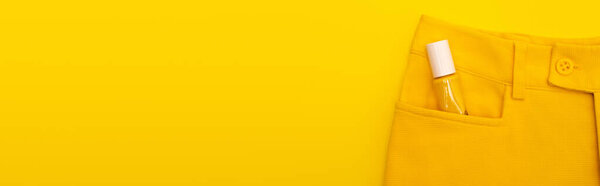верхний вид стеклянной бутылки с лаком для ногтей в кармане брюк изолированы на желтый, баннер