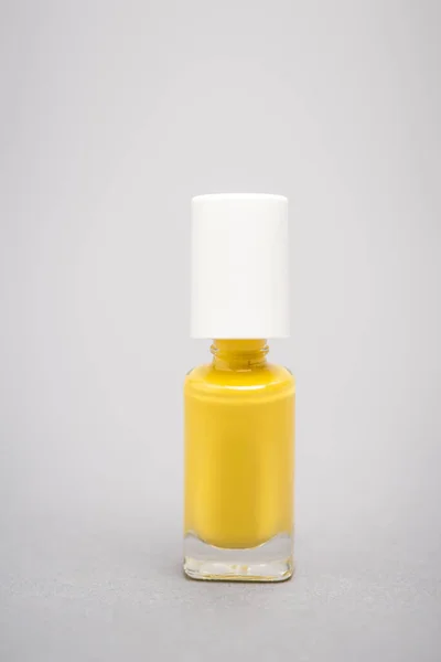 bottle with yellow nail polish on grey background