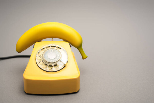 желтый банан на ретро-телефоне на сером фоне