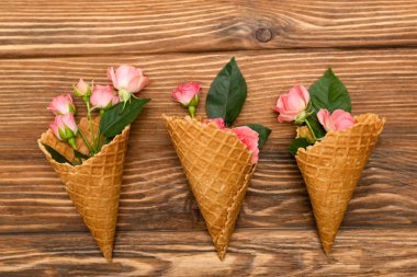 Ahşap yüzey üzerinde waffle konisi yapraklı pembe çay güllerinin üst görüntüsü