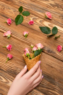 Waffle külahı ve ahşap yüzeyde pembe çay gülleri tutan bir kadın.