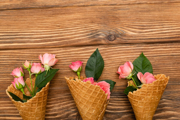 top view of pink tea roses in waffle cones on wooden surface
