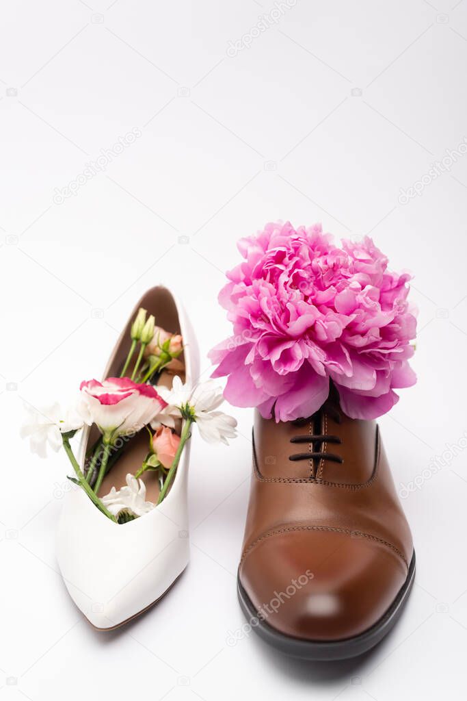 peony flower in male shoe near female footwear on white