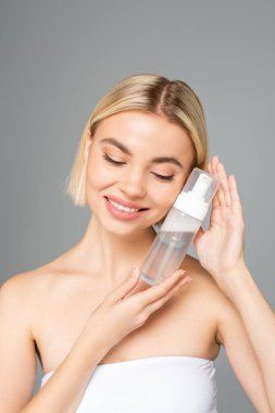 Mükemmel ciltli gülümseyen kadın gri renkte izole edilmiş köpük şişesi tutuyor. 