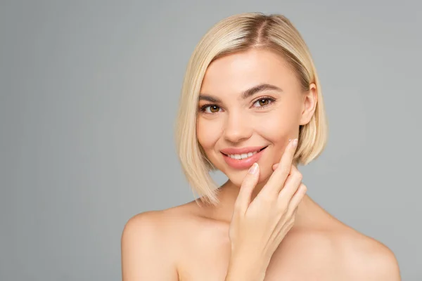 Glimlachende Blonde Vrouw Aanbrengen Cosmetische Crème Wang Geïsoleerd Grijs — Stockfoto