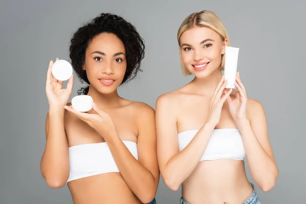 Sonrientes Mujeres Multiétnicas Sosteniendo Tubo Frasco Con Crema Cosmética Aislada — Foto de Stock