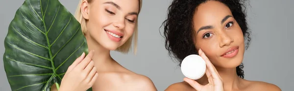Młode Wielokulturowe Kobiety Trzymające Krem Kosmetyczny Liść Tropikalny Wyizolowane Szarym — Zdjęcie stockowe