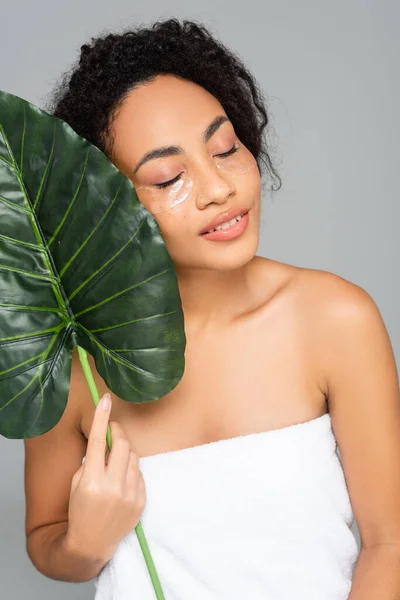 African american woman in eye patches holding green leaf isolated on grey