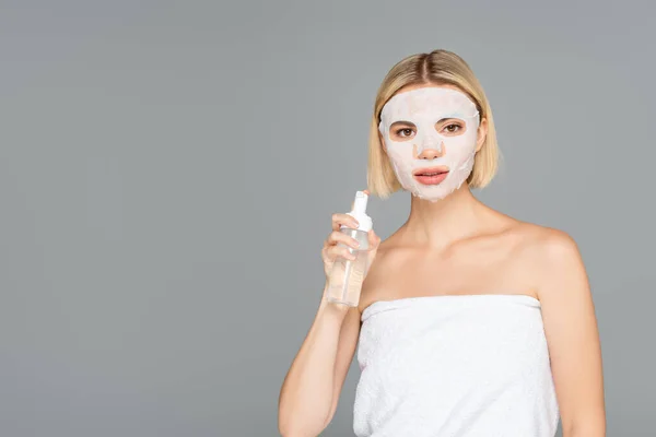 Young woman with sheet mask holding cleansing foam isolated on grey