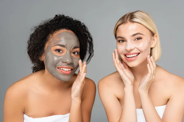 Alegres Mujeres Multiculturales Aplicando Máscaras Faciales Mirando Cámara Aislada Gris — Foto de Stock